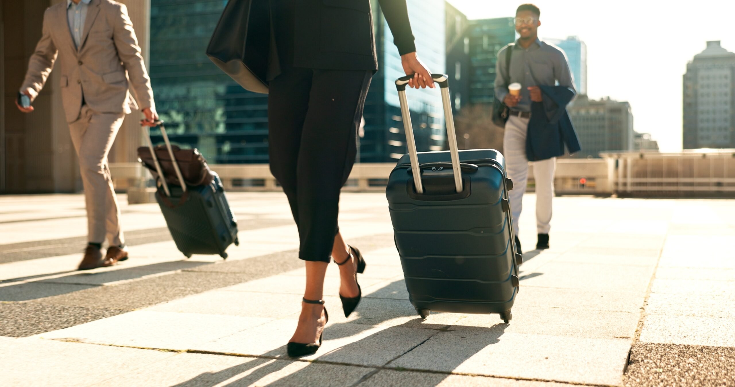 A businesswoman in heels wheeling her suitcase across a sunlit city plaza