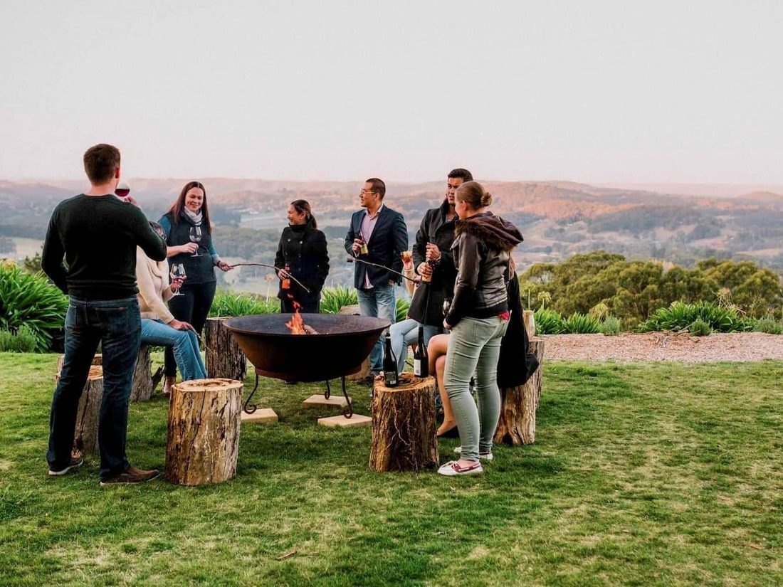 Friends gathered around a fire pit on a clifftop lawn