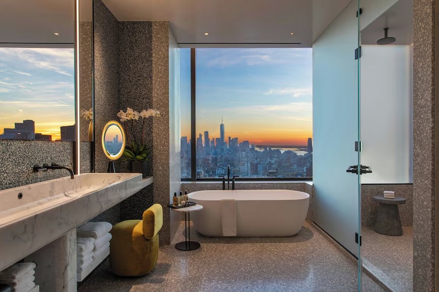 A marble bathroom with a freestanding tub facing the Manhattan skyline at sunset