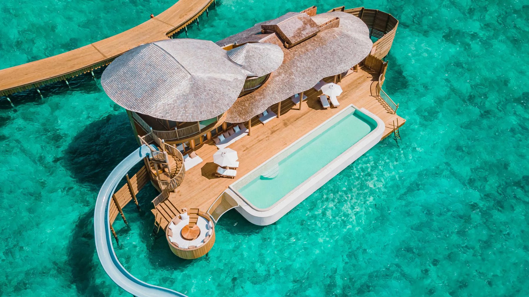 An overwater villa with a private pool and slide in a turquoise lagoon